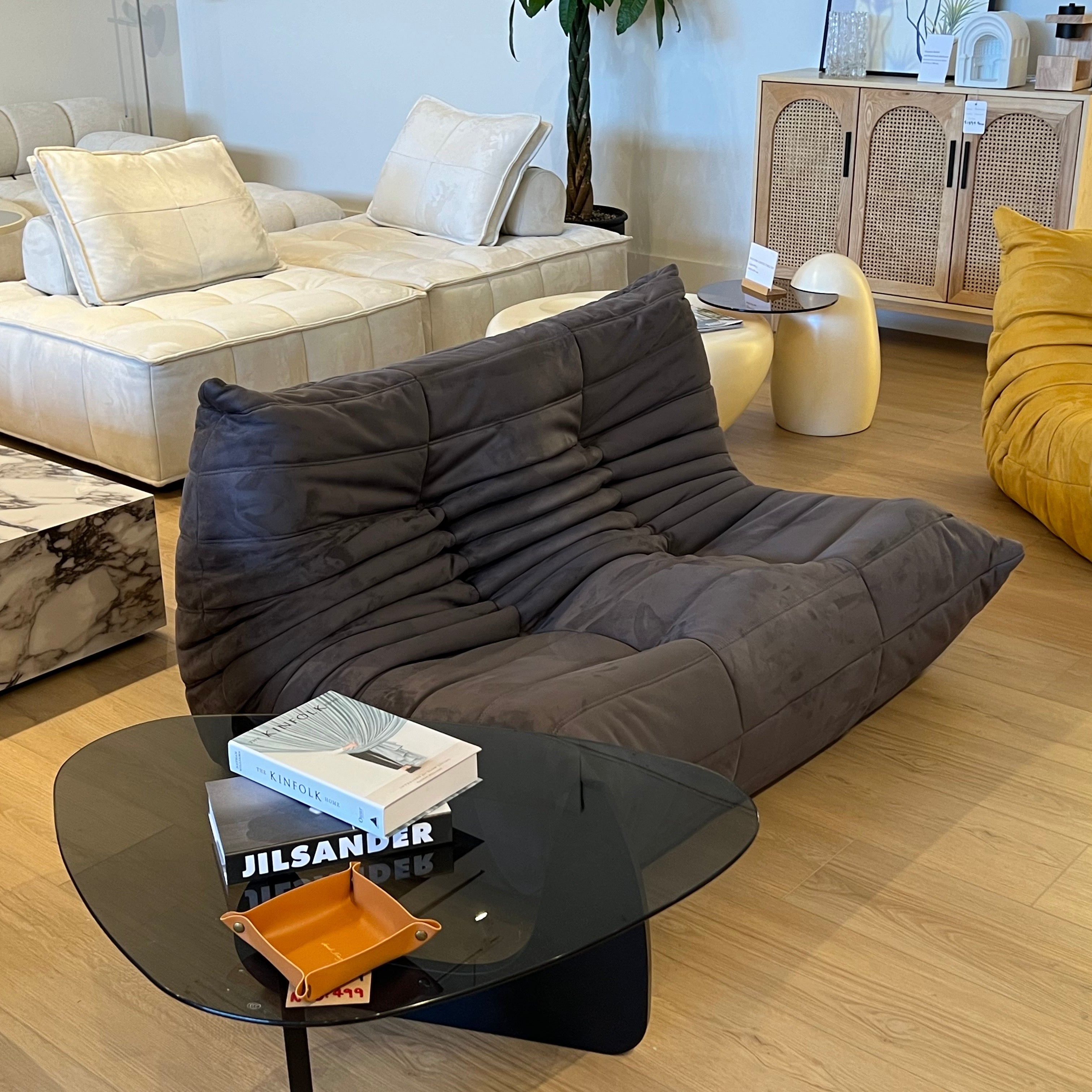 A dark gray, caterpillar-shaped sofa with deep, segmented cushions is the focal point of this modern furniture showroom.