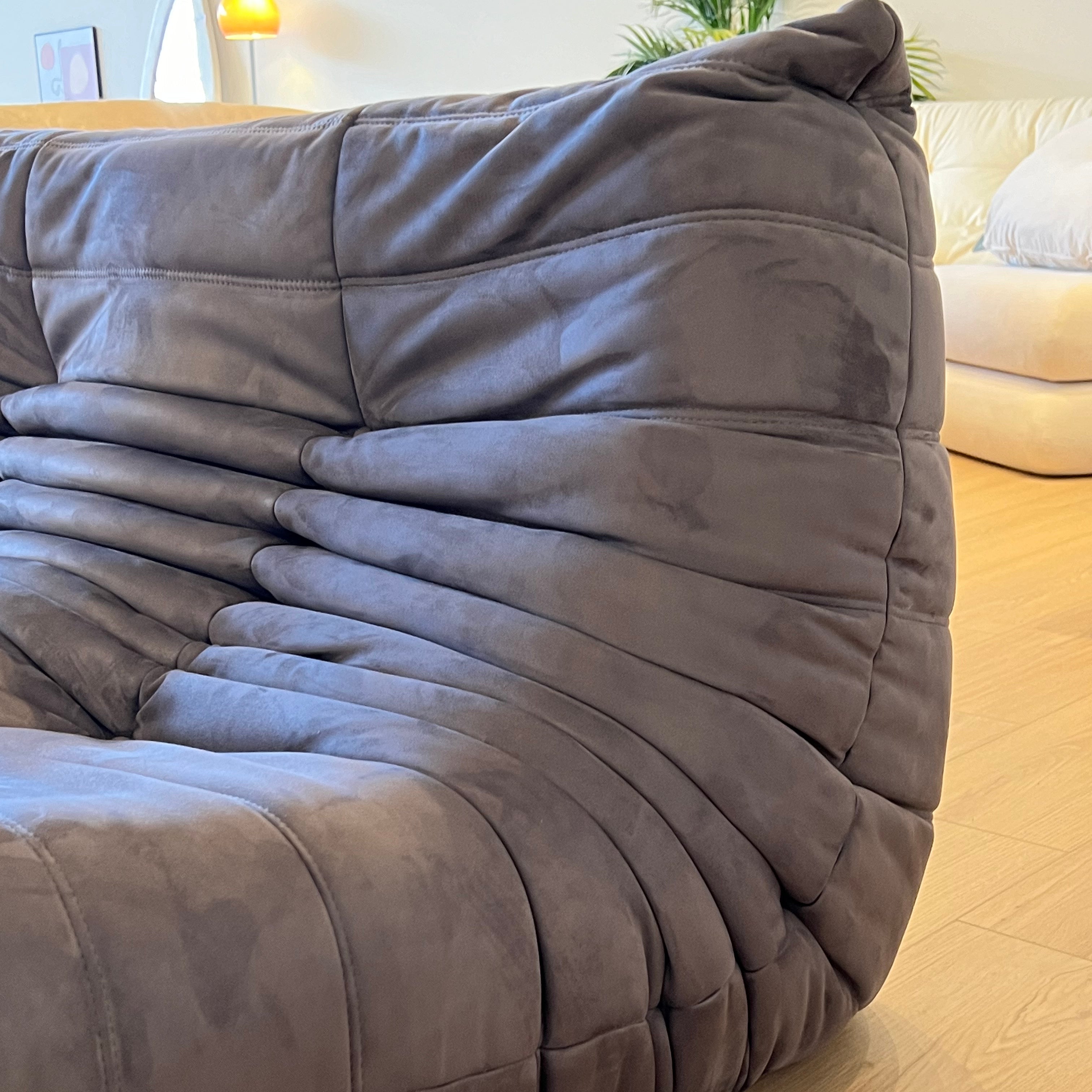 A close-up view of a dark gray, caterpillar-shaped sofa with deep, segmented cushions.