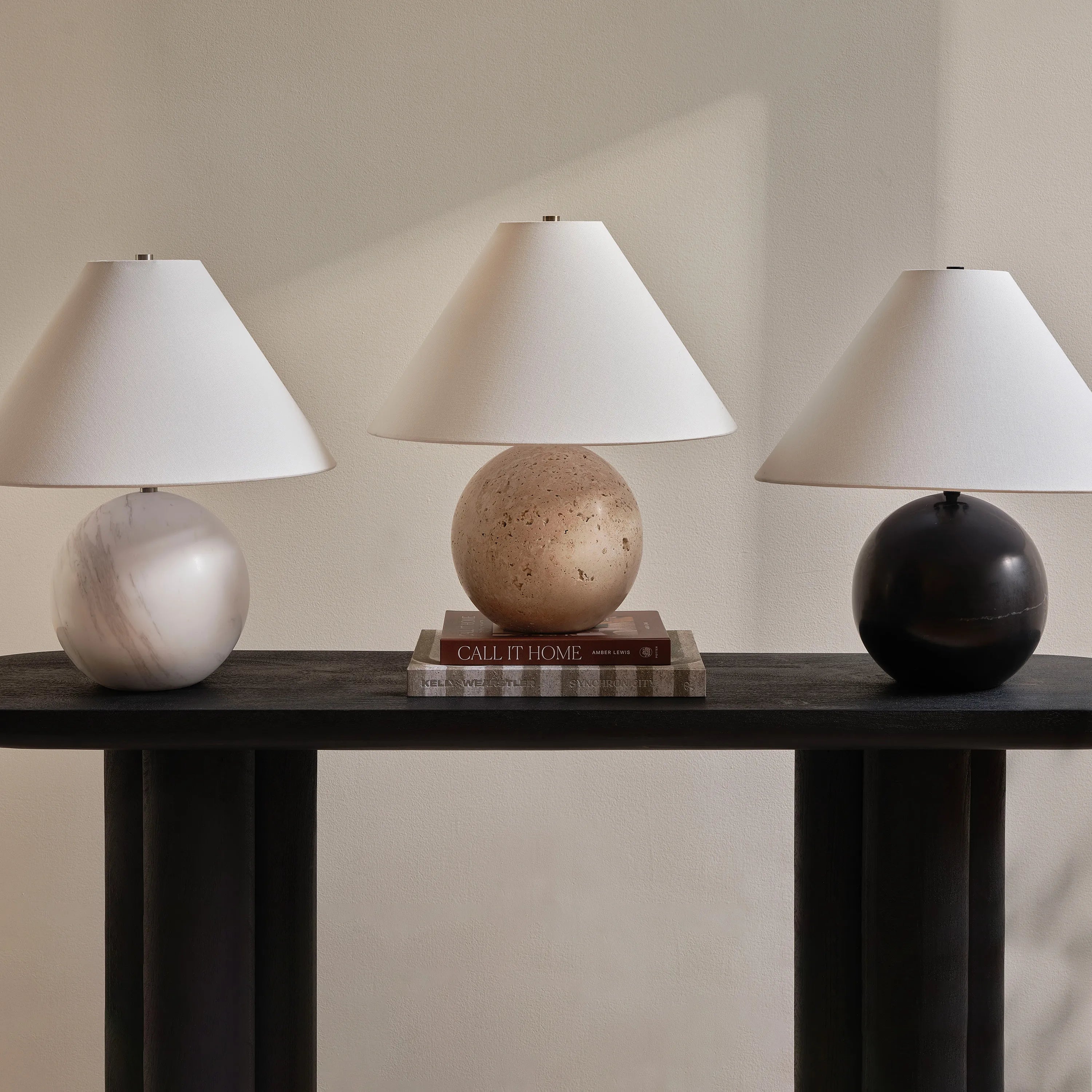 Arlo Sphere Table Lamps in white marble, travertine, and black marble displayed on dark console table with neutral backdrop