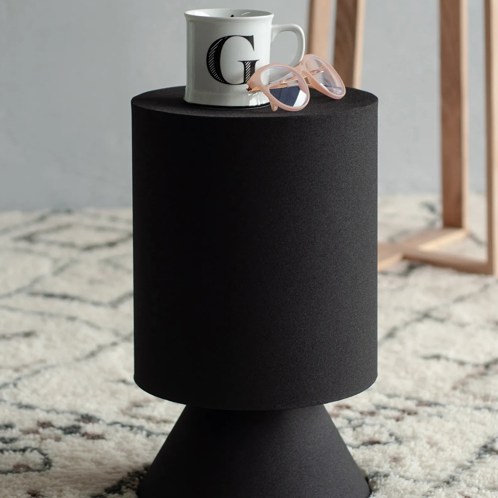 Atlas black sculptural side table styled on a textured rug with a coffee mug and glasses, showcasing its functional surface area.