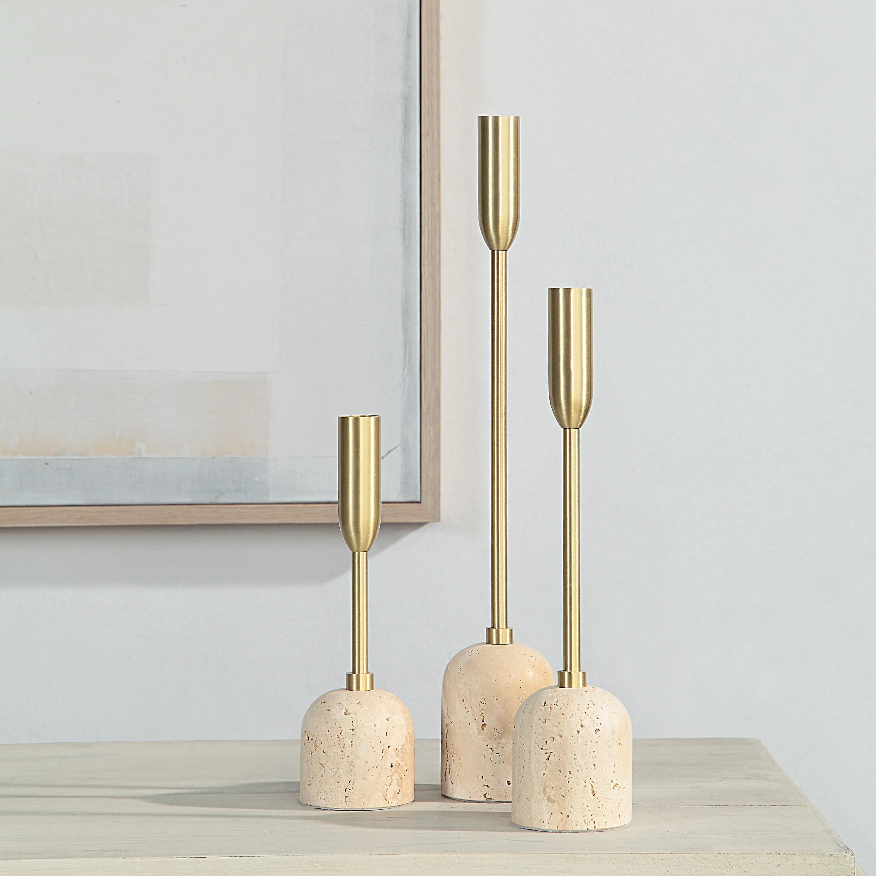 Set of Aurelia Candle Holders with brass stems and travertine bases displayed on a light wood table against a neutral wall