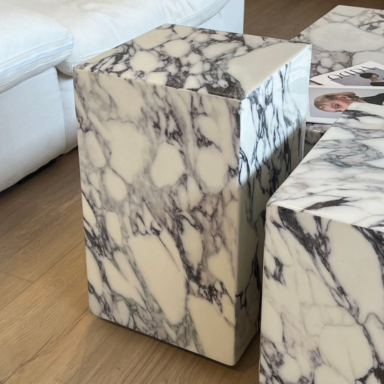 Close-up of Bulgari Charm Coffee Table pedestal in polished white marble with dark veining beside cream modular sofa