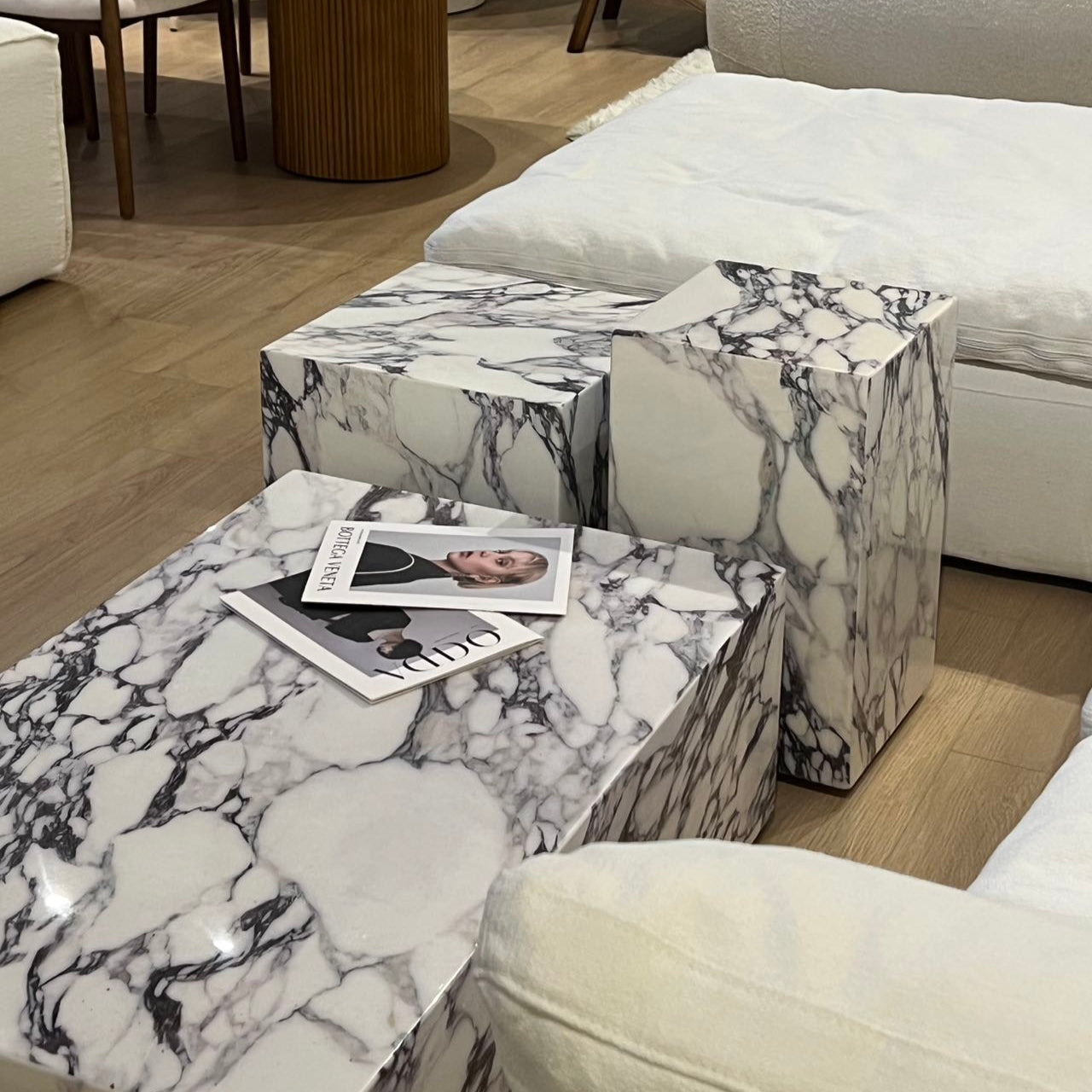 Bulgari Charm Coffee Table set in white marble with dark veining styled beside white sofa on wood flooring