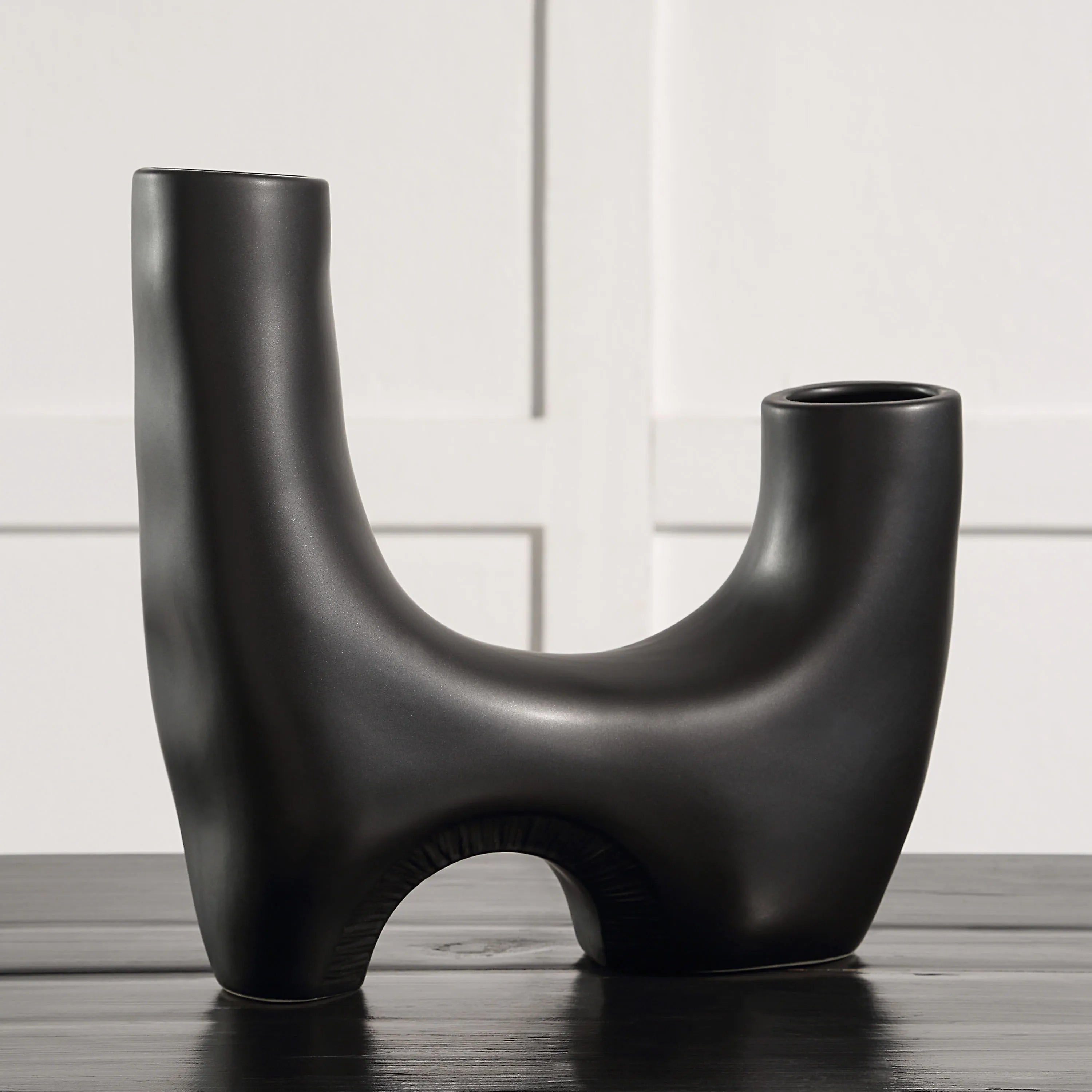 Caldera Vase in matte black finish displayed on table against white wall panel backdrop