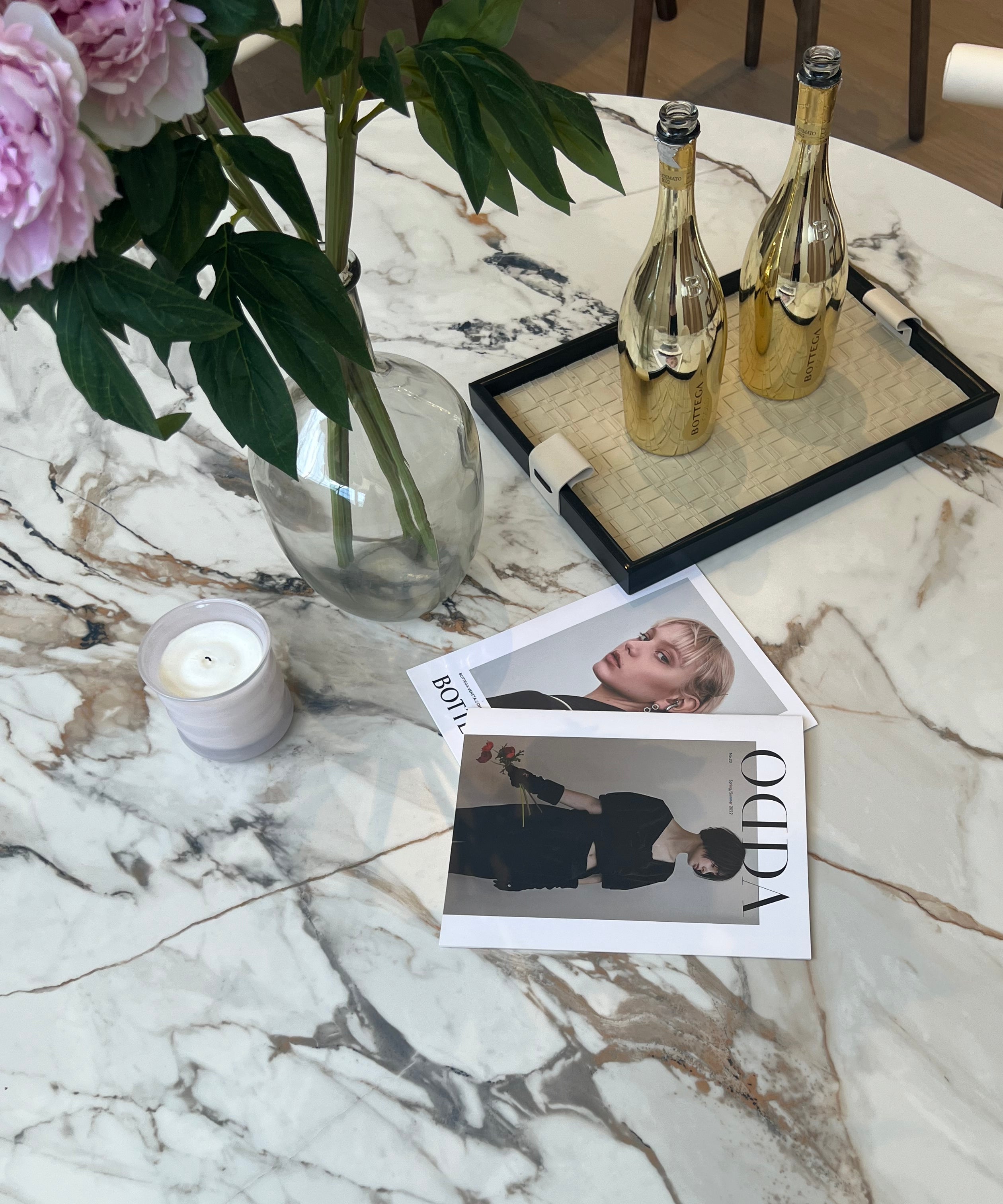 Close-up of Celesti Elegance round dining table with marble-patterned sintered stone top styled with flowers, magazines, and gold bottles