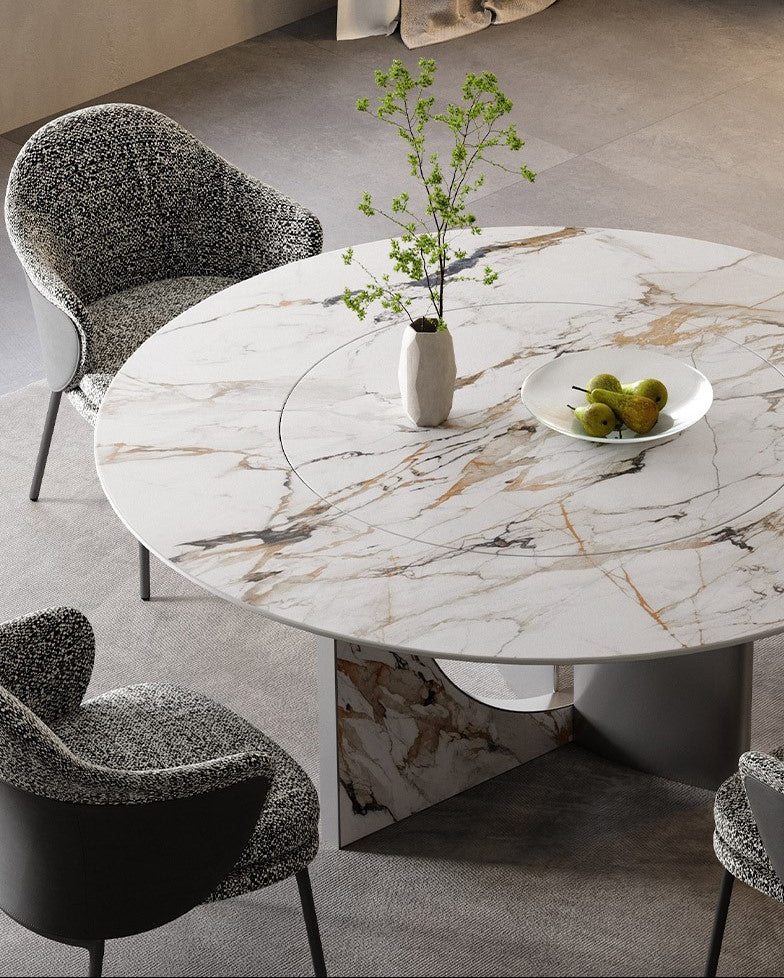 Celesti Elegance round dining table with marble-patterned sintered stone top and stainless steel base, decorated with vase and fruit bowl
