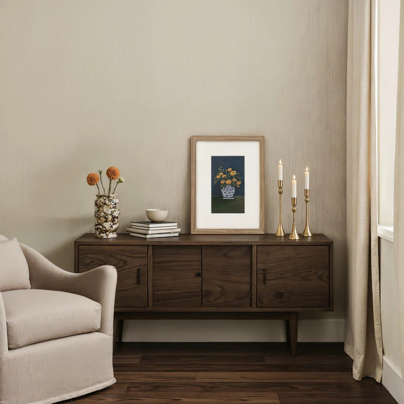 The Clementine framed floral wall art styled on a dark wood sideboard next to brass candlesticks and a cream armchair.