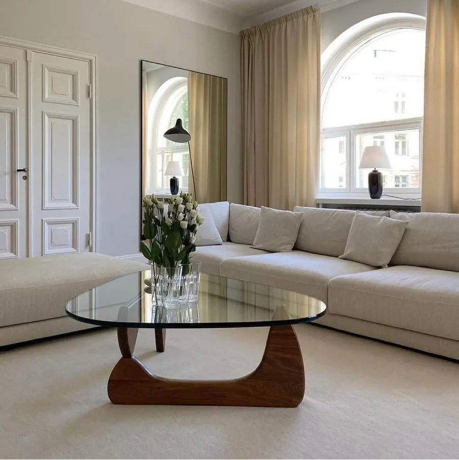 Contour Glass Coffee Table with round glass top and sculpted walnut base styled in a bright neutral living room