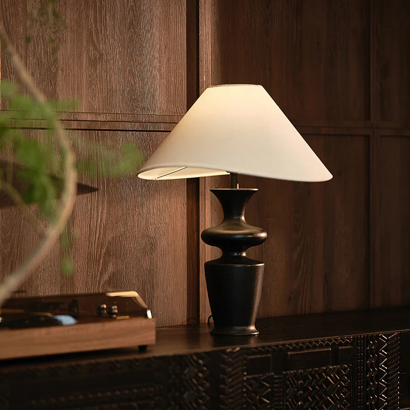 "Contour Table Lamp with black sculpted base and white shade on dark cabinet against wood-paneled wall