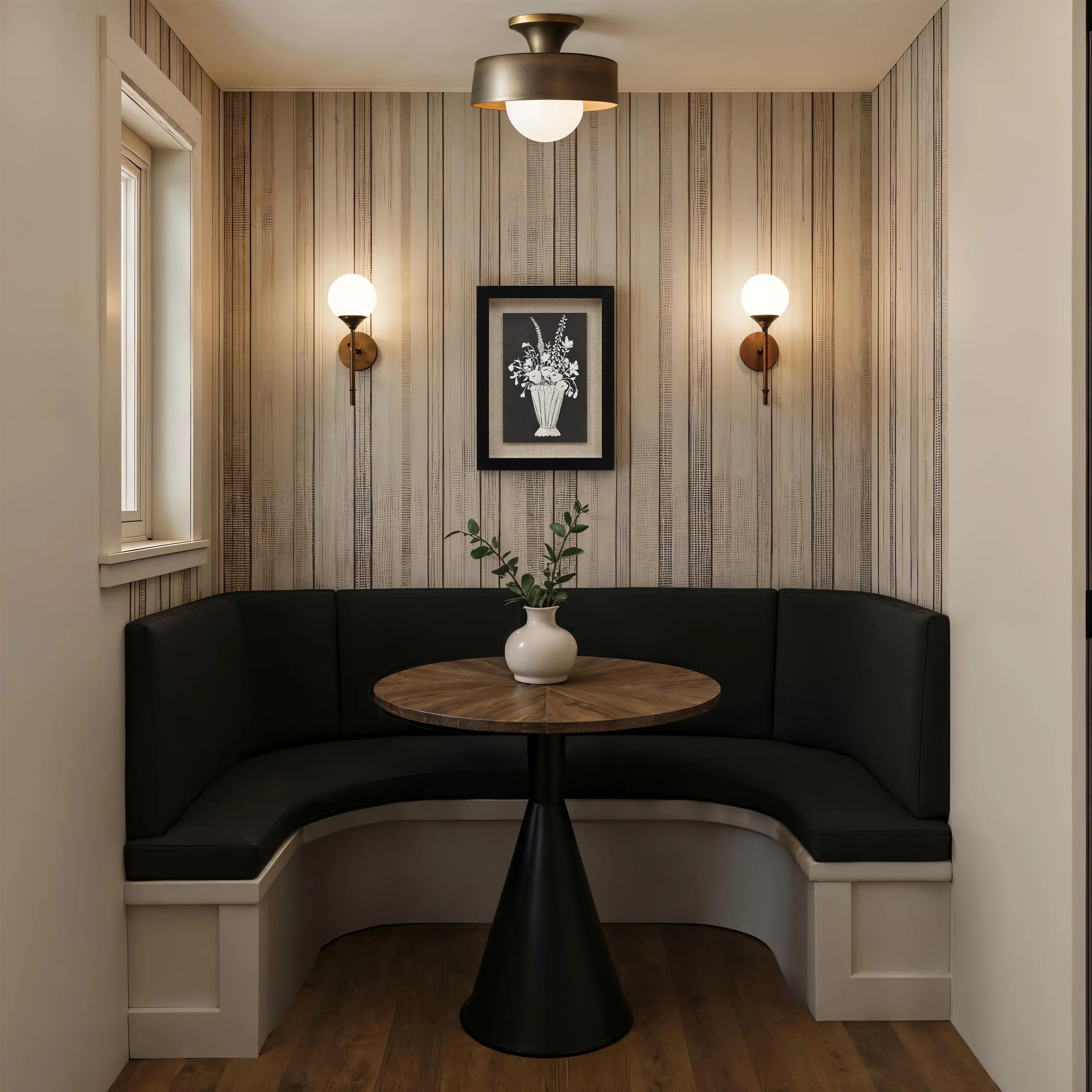 The Daphne botanical wall art hanging above a dark corner banquette seating area with a round wooden table and wall sconces.