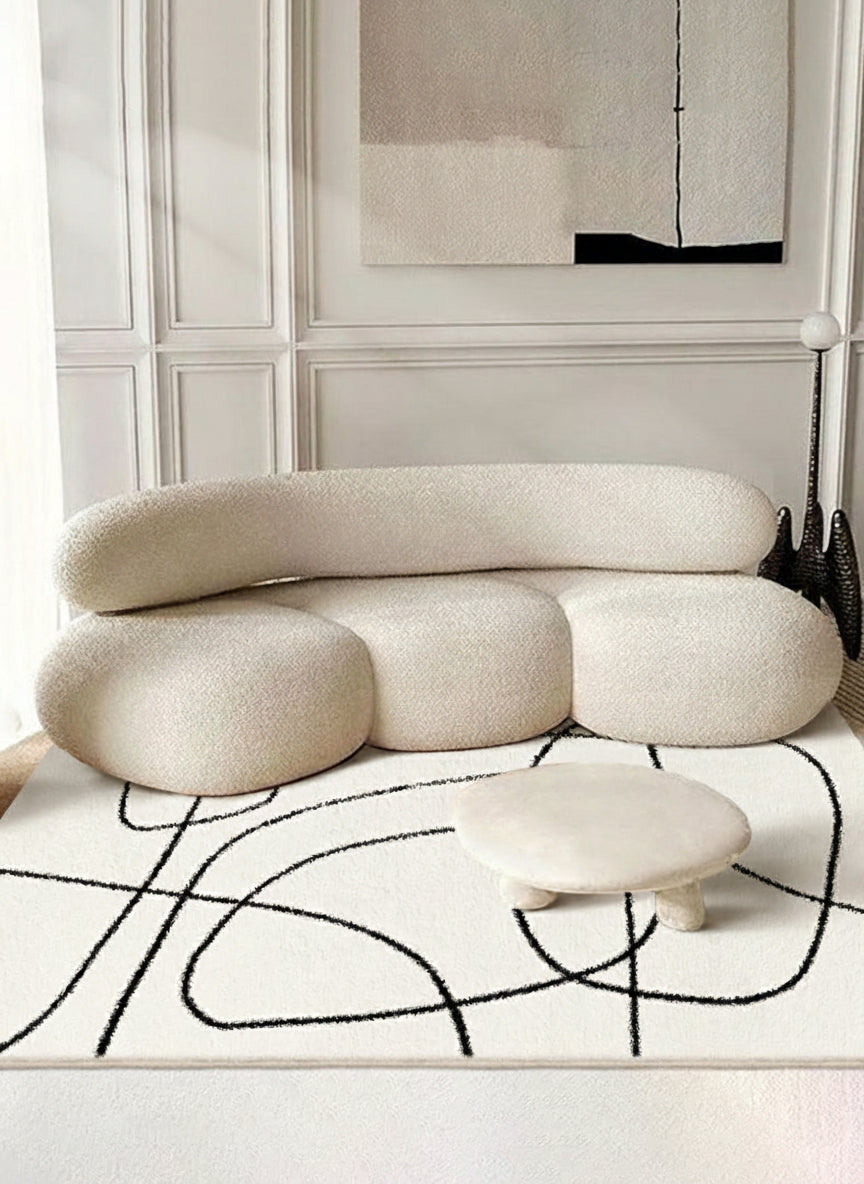 Eclipse Black and White Abstract Rug styled with a modern cream curved sofa and round low table in a bright living room