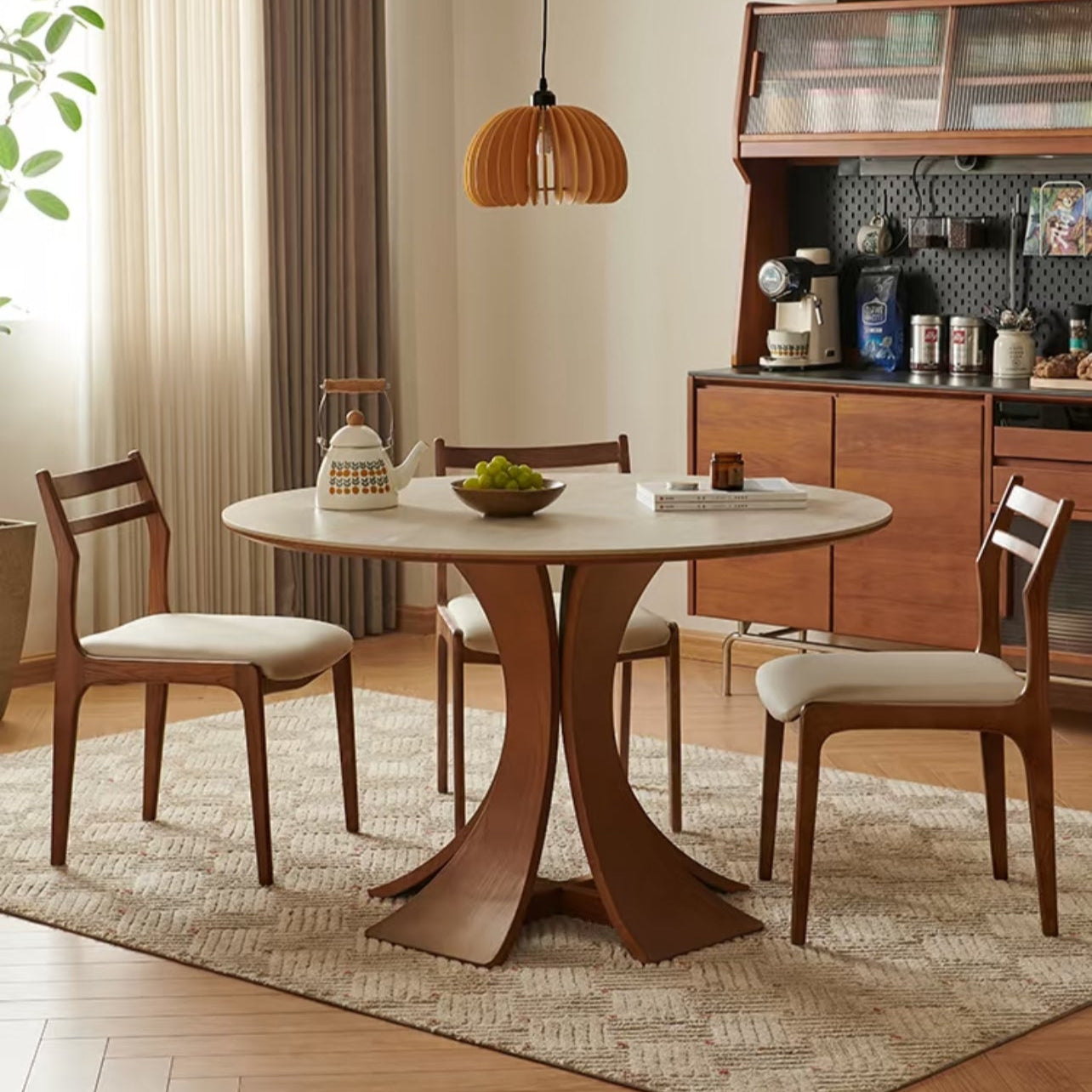 Elowen Round Dining Table with walnut base and matching chairs in warm dining space with pendant light and sideboard