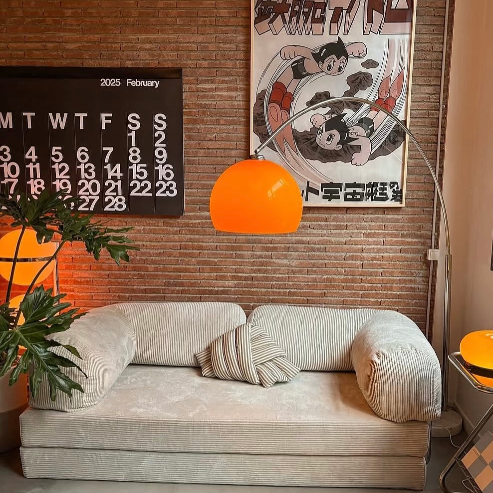 Goldenhour Adjustable Arc Floor Lamp with orange shade illuminating a cozy living room with retro art and beige sofa