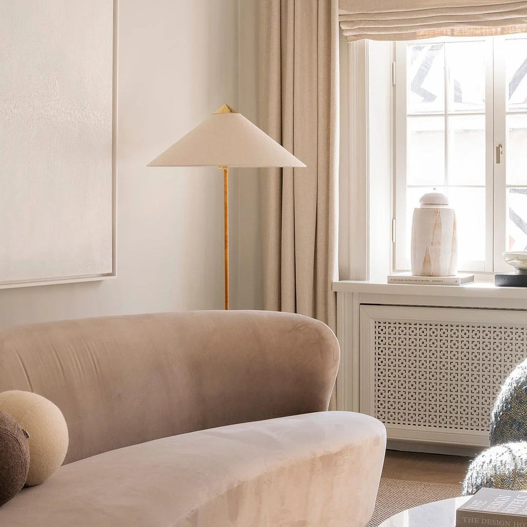 Horizon Shade Floor Lamp with brass stand and wide cone shade placed beside a curved beige velvet sofa in cozy living room