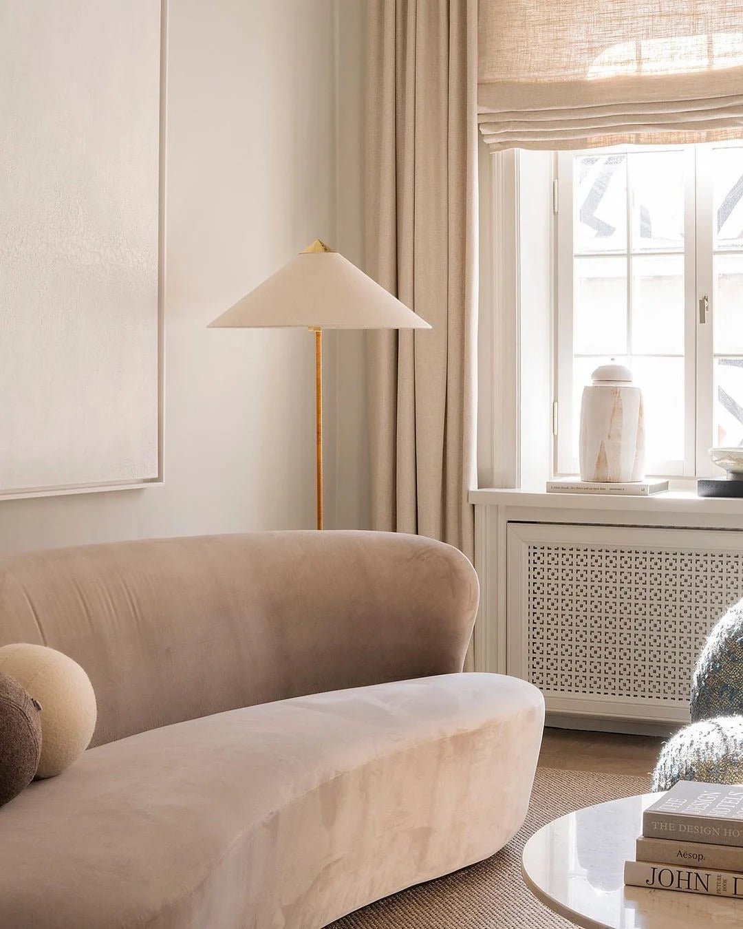 Horizon Shade Floor Lamp with brass stand and wide cone shade placed beside a curved beige velvet sofa in cozy living room