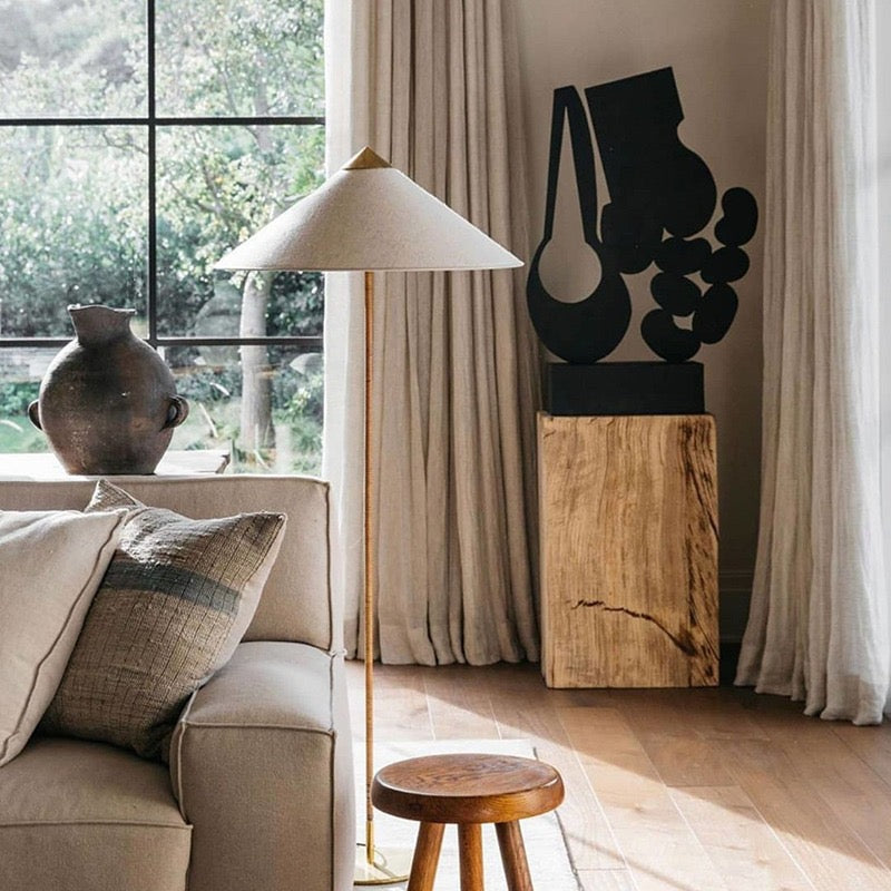 Horizon Shade Floor Lamp with brass stand and wide cone shade beside beige sofa in sunlit living room