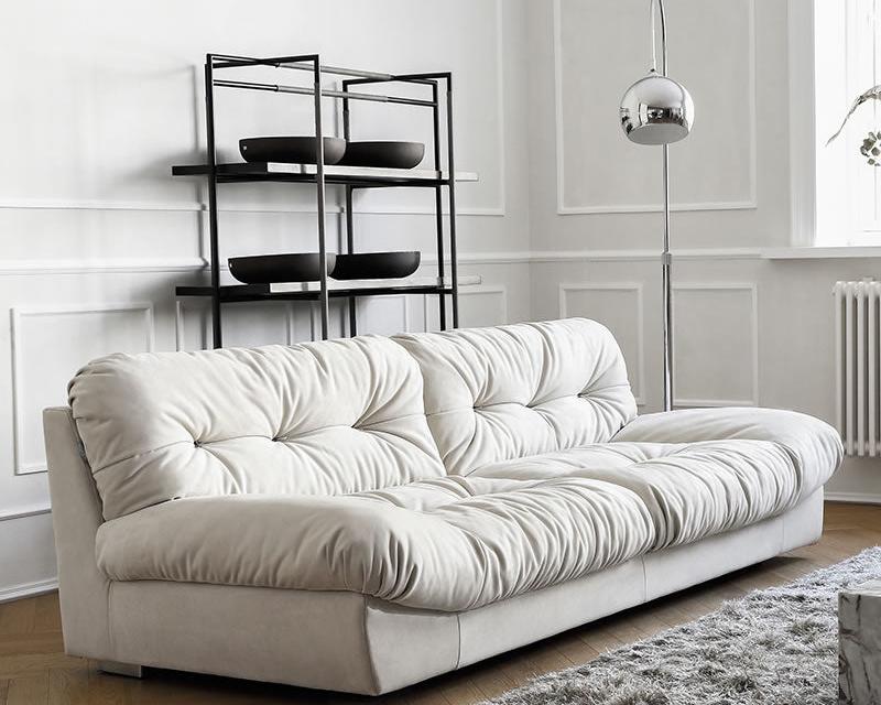 Italian-style Cloud Sofa in cream ultra suede with deep tufted cushions, shown in a modern living room with black shelving and floor lamp