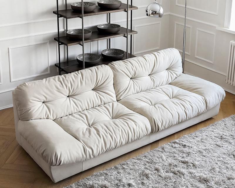 Italian-style Cloud Sofa in cream ultra suede with deep tufted seat and back cushions, styled in a modern living room with shag rug and shelving