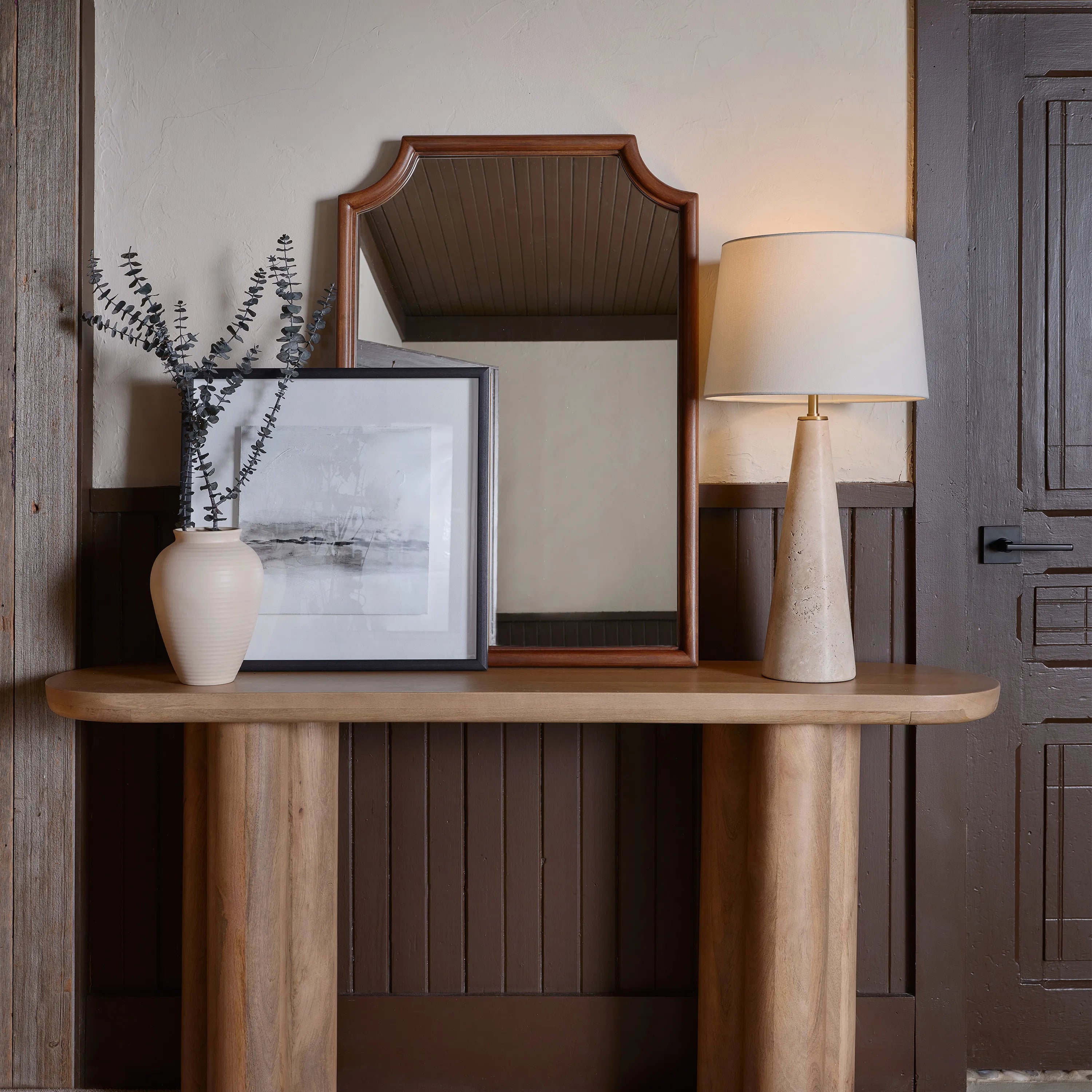 Marlo Travertine Table Lamp on wooden console beside framed art and ceramic vase in warm neutral entryway