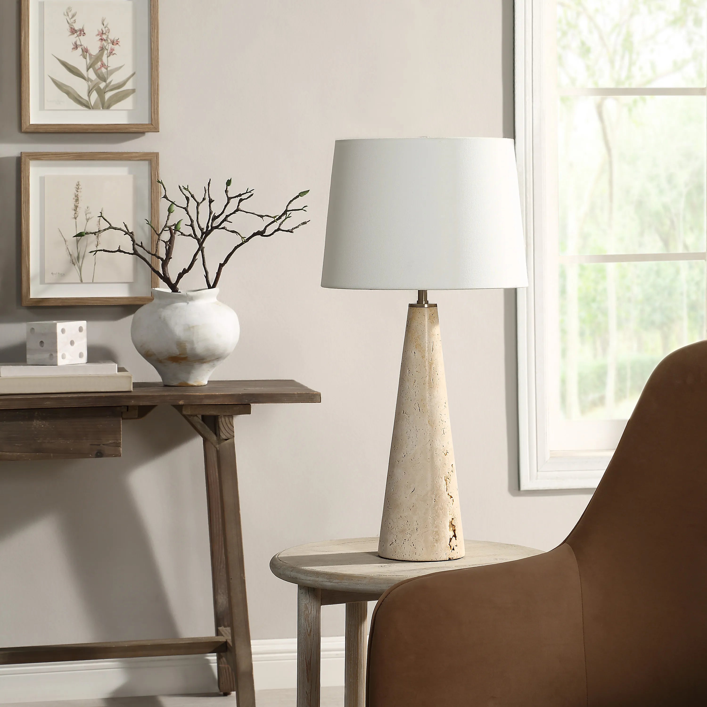 Marlo Travertine Table Lamp on round side table beside brown chair and wooden console in cozy living room
