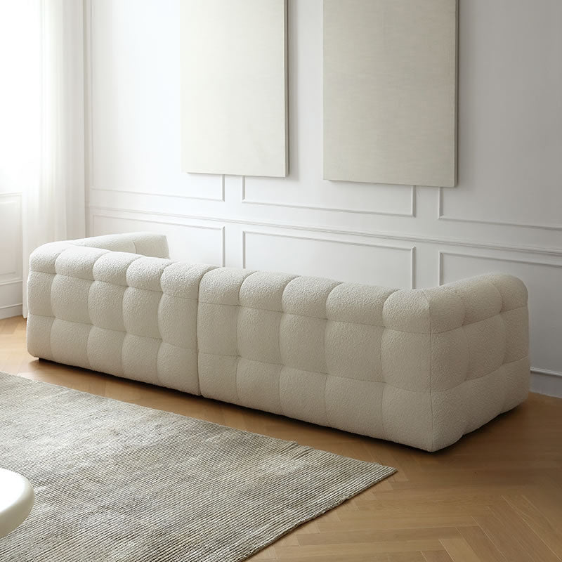 Back view of cream bouclé modular sofa with cube tufting in a bright living room with beige rug and wood flooring