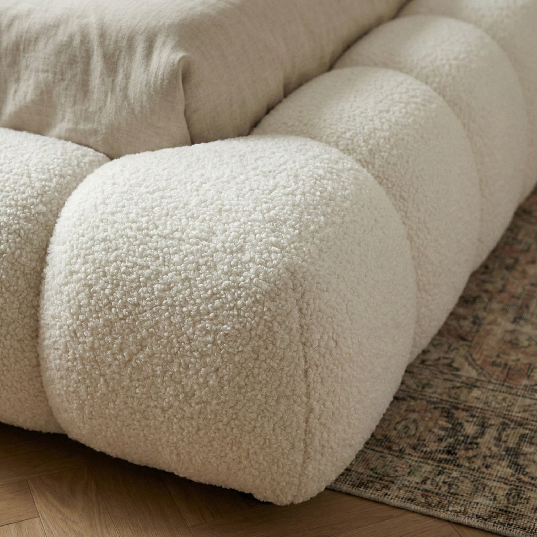 Close-up of a textured beige sofa with a patterned rug underneath.