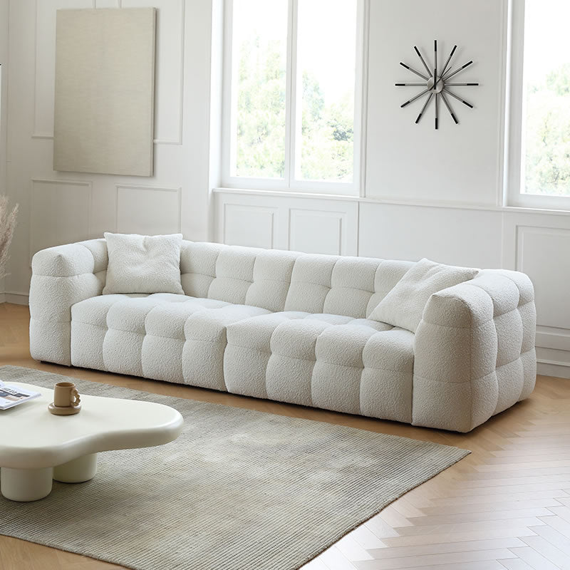 Modern cream bouclé modular sofa with cube tufting and pillows in a bright living room with wall clock and beige rug