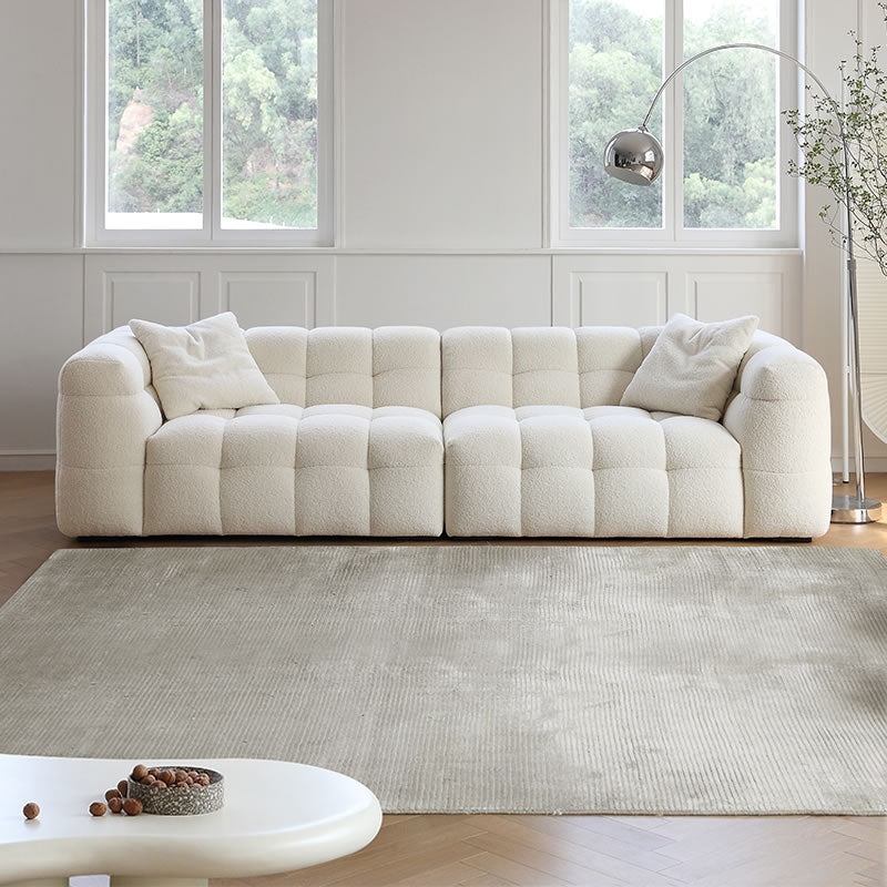 Cream bouclé modular sofa with cube tufting and pillows in a bright living room with large windows and beige rug