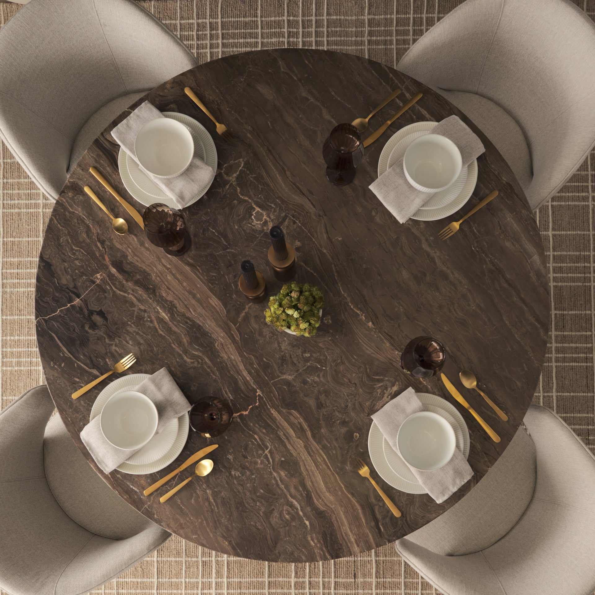Overhead bird's-eye view of the Mateo round brown marble table styled with a complete dinnerware set for four and gold cutlery.