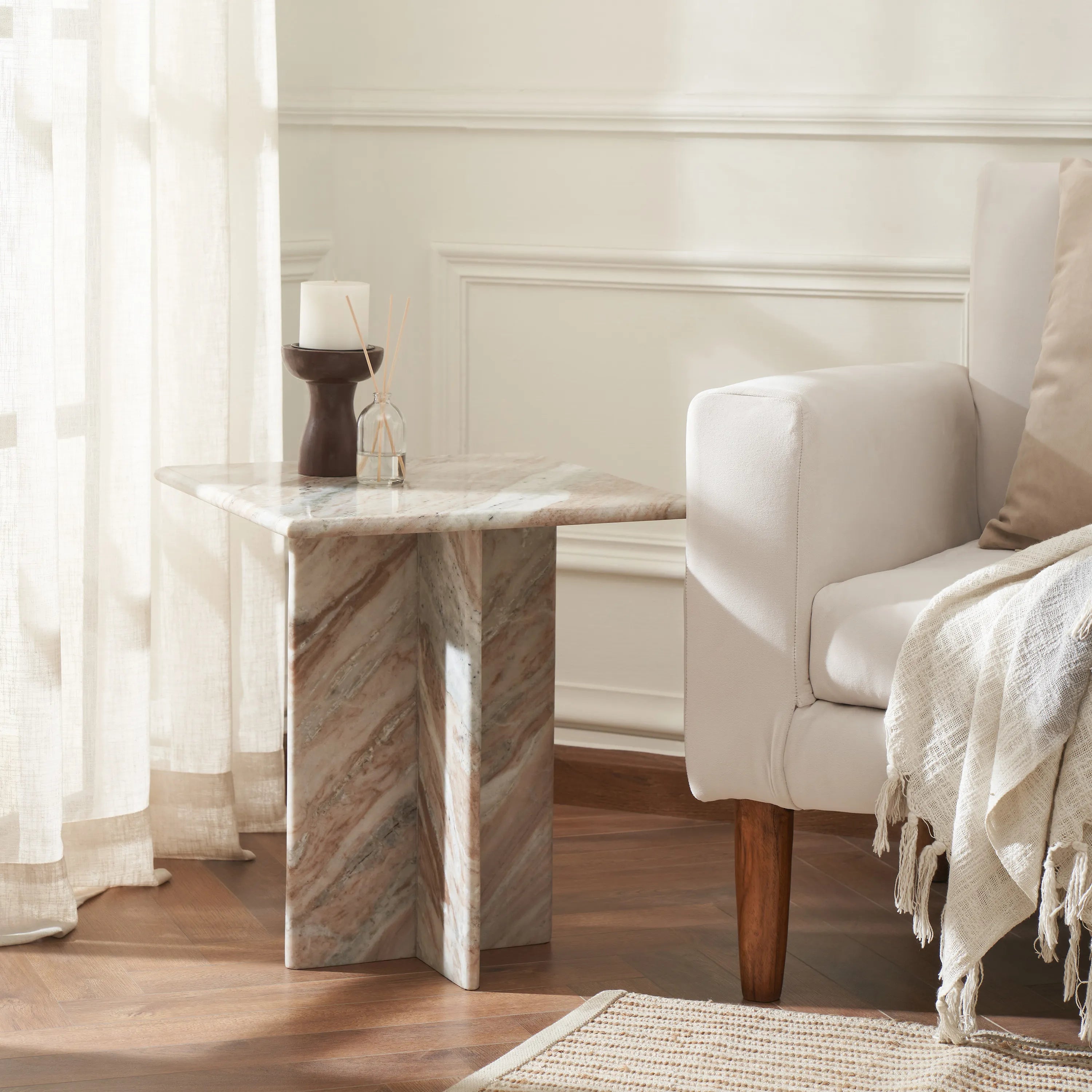 Mesa marble end table styled next to a cream armchair in a sunlit living room, highlighting the warm tones of the natural stone.
