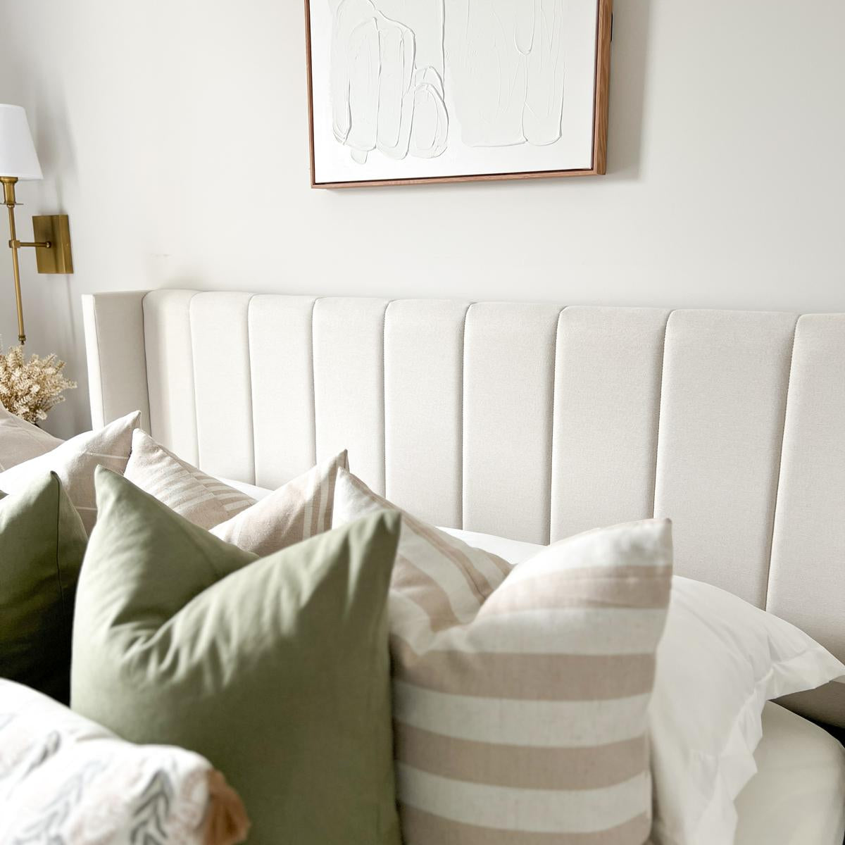 Close-up of the soft cream upholstery and vertical channeling on the Mila bed headboard, styled with olive green and striped neutral throw pillows.