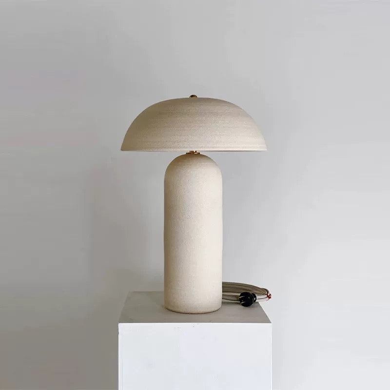 Mira Ceramic Table Lamp with rounded base and dome shade displayed on white pedestal in minimal studio setting