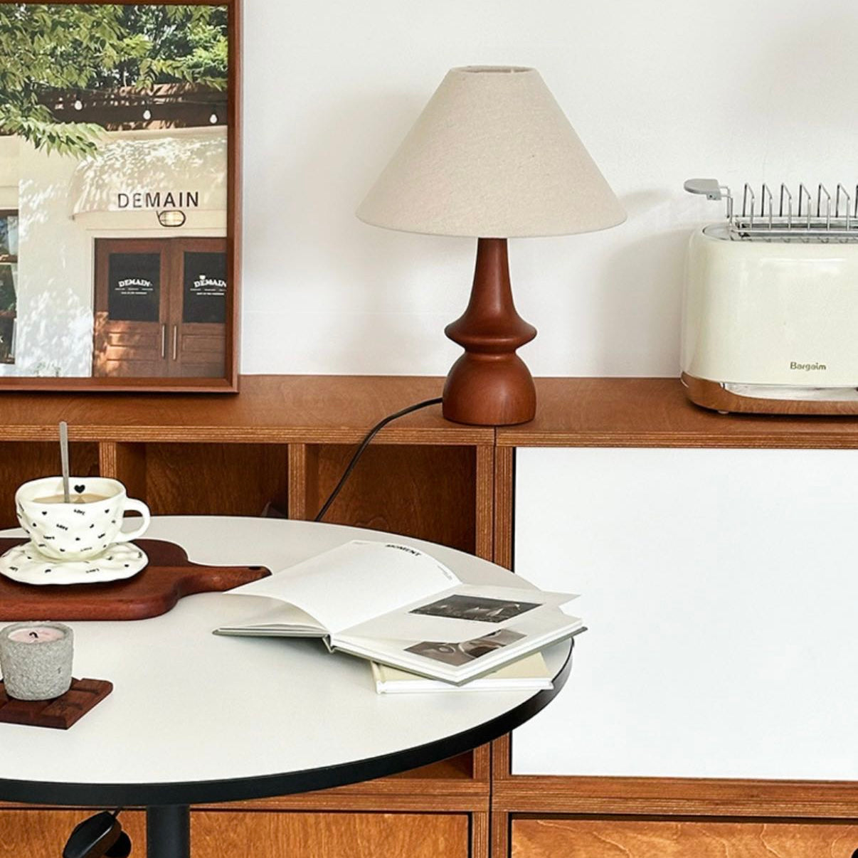 Olivia Table Lamp with walnut base placed on a wooden sideboard beside a table with cup and book