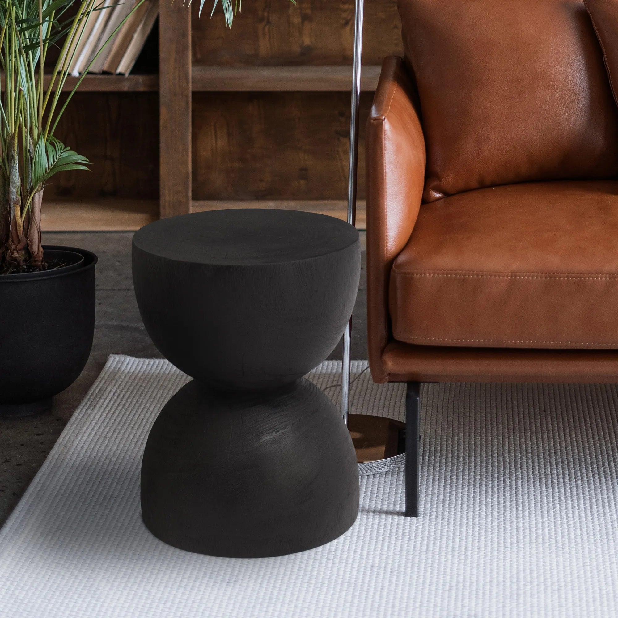 Onda black wood side table styled next to a leather armchair, highlighting its organic totem design and modern aesthetic.