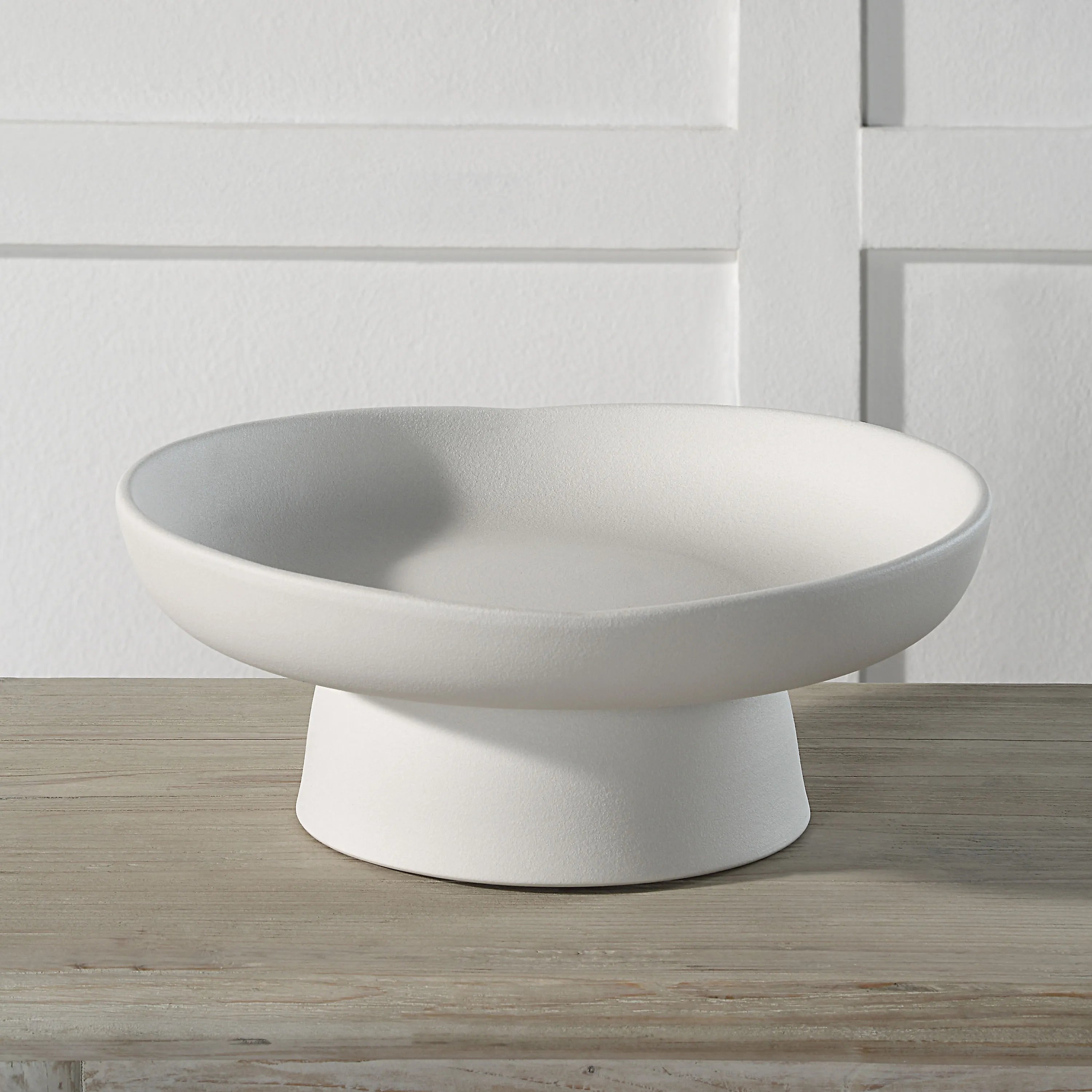 Orla Ceramic Bowl in matte white finish displayed on a wooden table against a paneled white wall