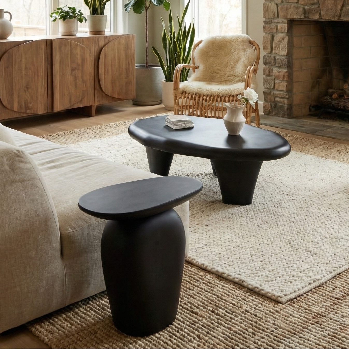 Organic black pebble tables styled in a bright rustic living room with a stone fireplace, jute rug, and rattan chairs.