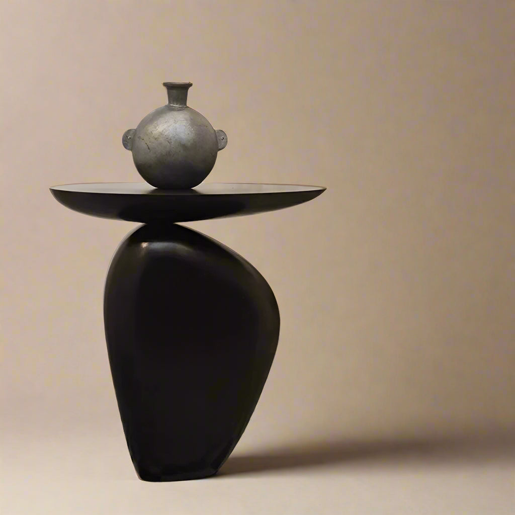 Pebble Side Table in matte black finish displayed in minimalist studio setting with sculptural vase on top