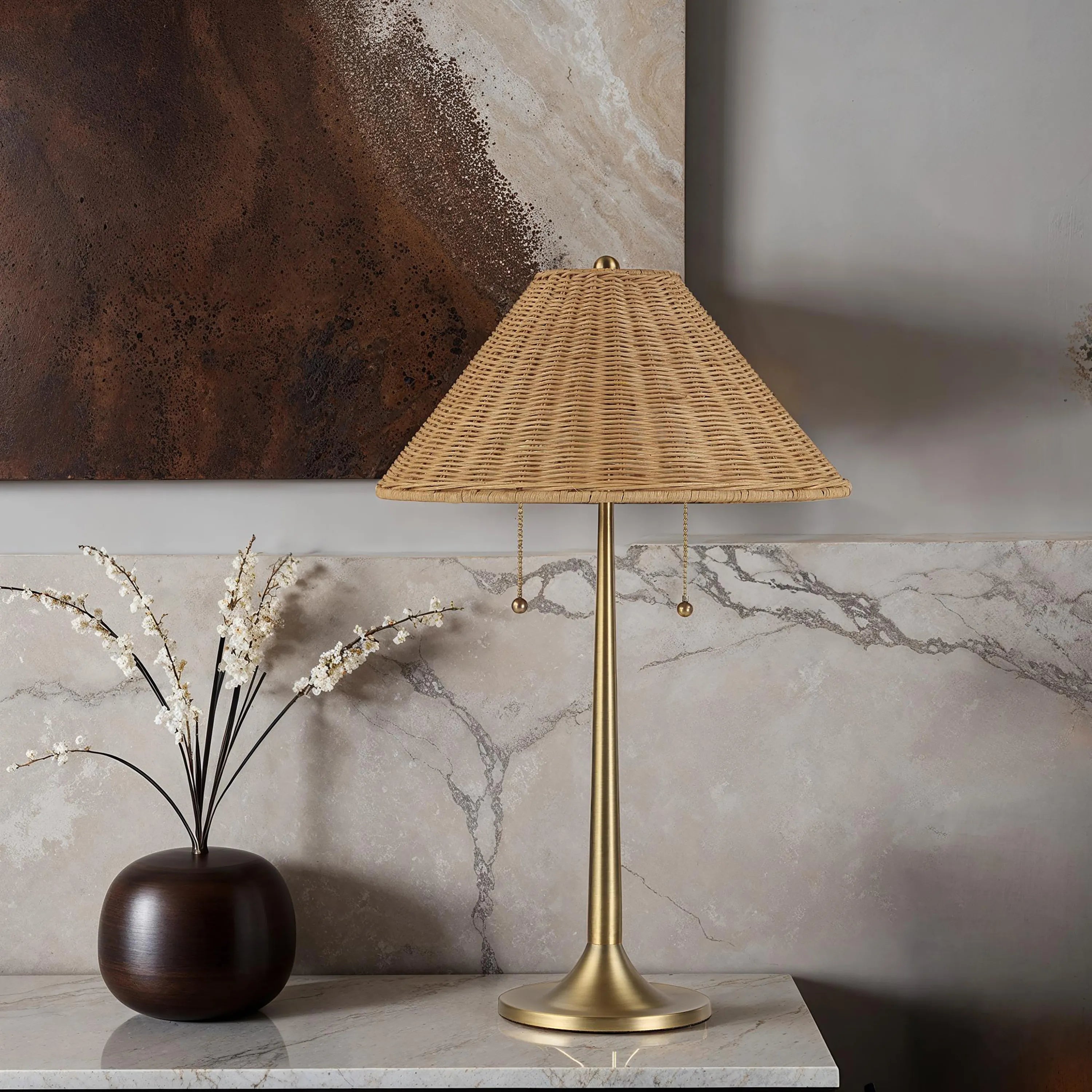 Solara Rattan Glow Table Lamp with brass base and rattan shade on marble console beside dark vase decor