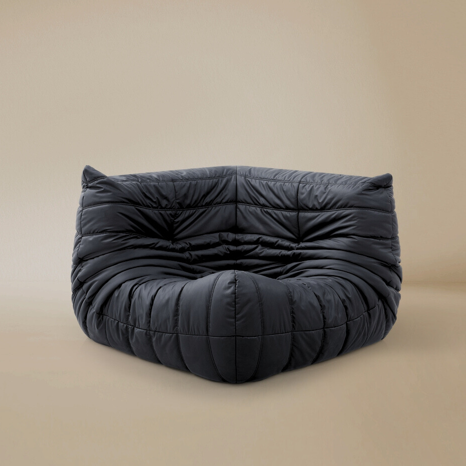 Dark grey TOGO Lounger corner chair showing deep tufted folds and low profile floor seating design.