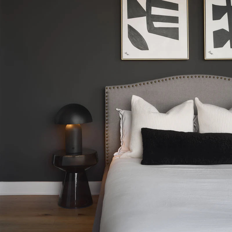 Umbra black dome lamp styled on a black side table in a moody modern bedroom with a grey upholstered bed.