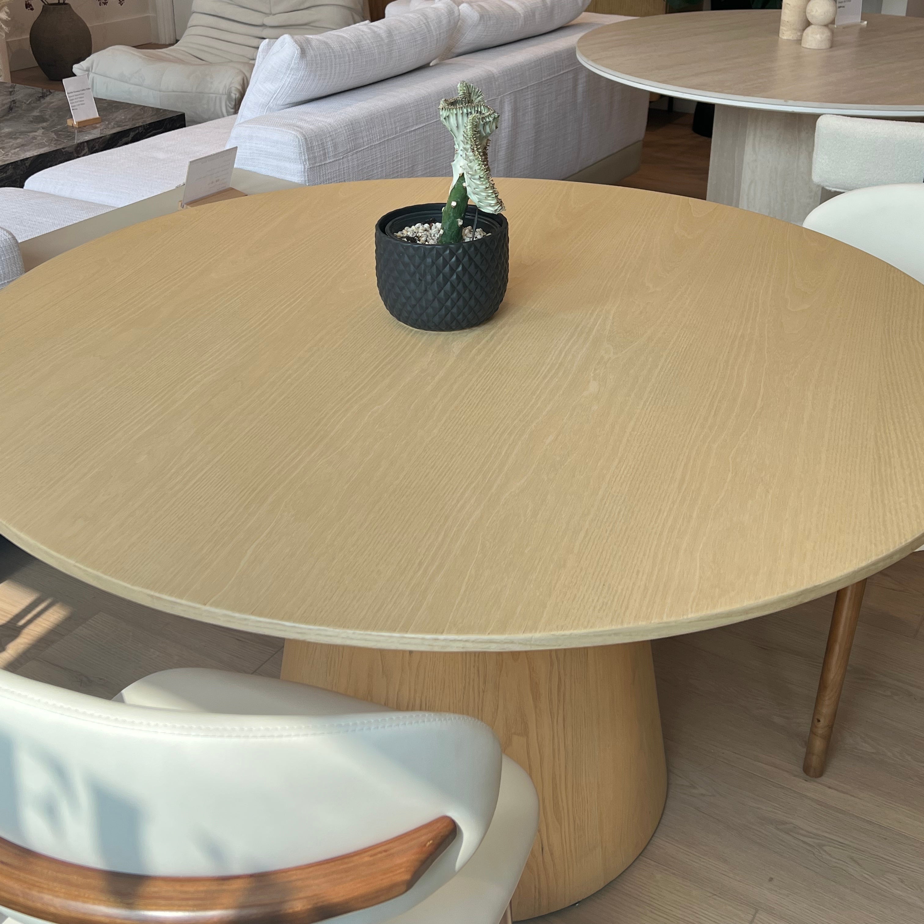 Willow Ridge round dining table in solid ash wood displayed in showroom with cream chairs