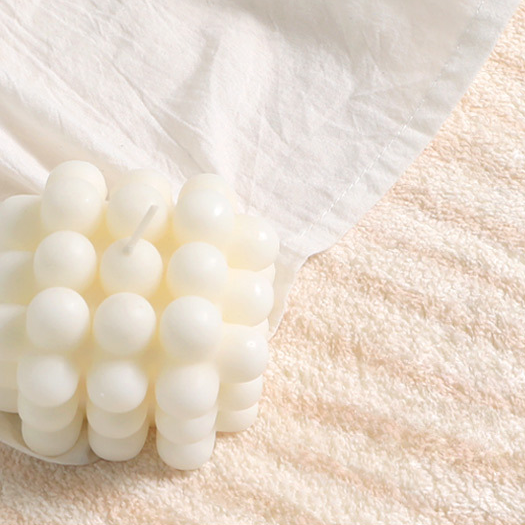 Lifestyle close-up of the Woven Whisper Rug with a white bubble candle and fabric placed on its plush beige texture.