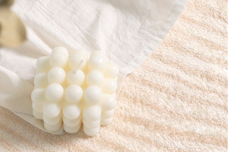 Lifestyle close-up of the Woven Whisper Rug with a white bubble candle and fabric placed on its plush beige texture.