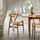 Alden Wishbone Dining Chair in a natural wood finish, styled in a minimalist dining room with a woven seat and soft neutral décor