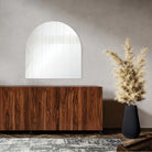 Arco Wall Mirror displayed above a wooden sideboard in a modern living room with a tall black vase and neutral decor