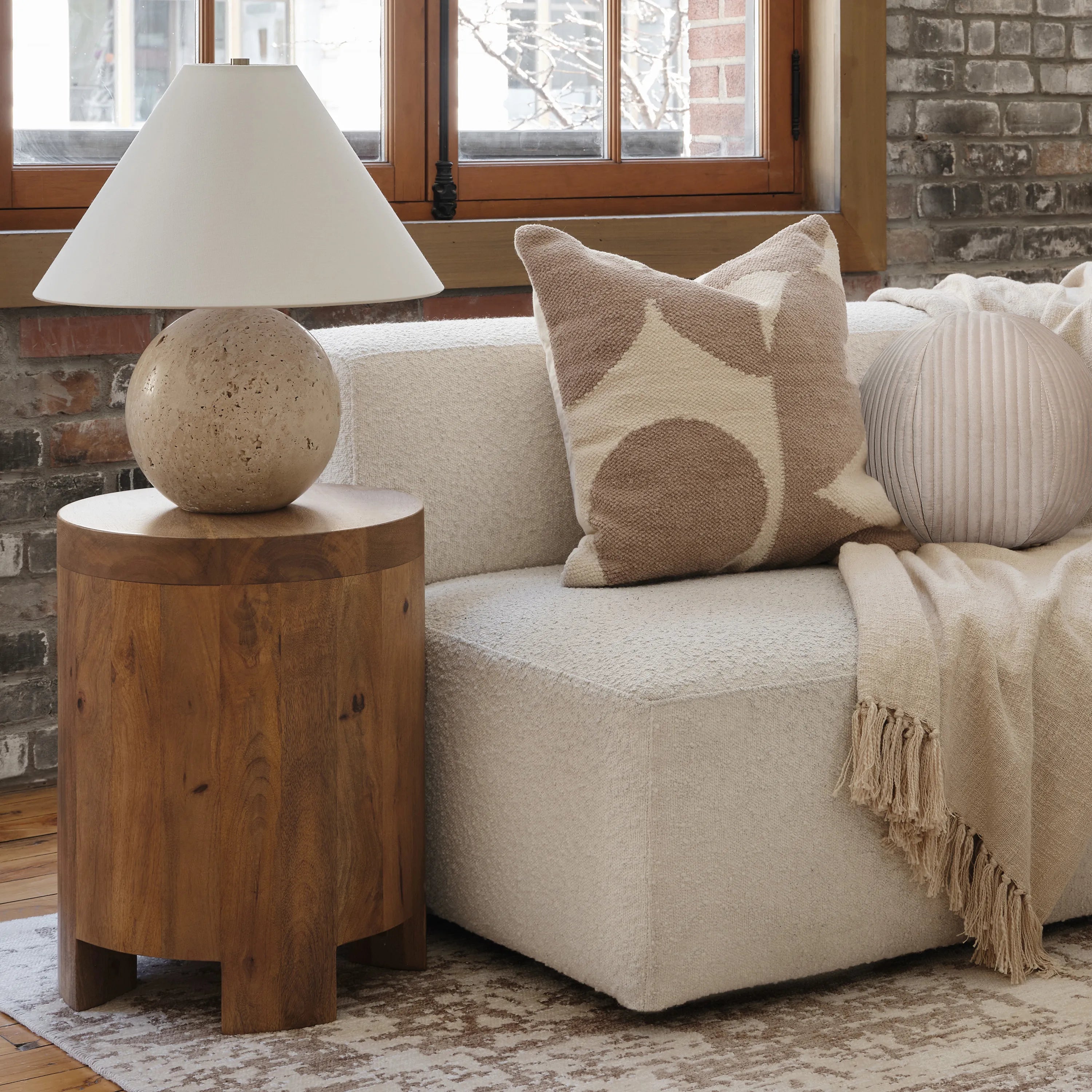 Arlo Sphere Table Lamp with travertine stone base on wooden side table beside cream sofa and neutral throw pillows
