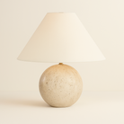 Arlo Sphere Table Lamp with natural travertine stone round base and wide tapered white fabric shade on beige background