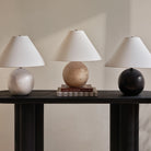 Arlo Sphere Table Lamps in white marble, travertine, and black marble displayed on dark console table with neutral backdrop