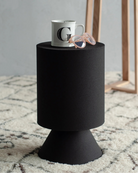 Atlas black sculptural side table styled on a textured rug with a coffee mug and glasses, showcasing its functional surface area.