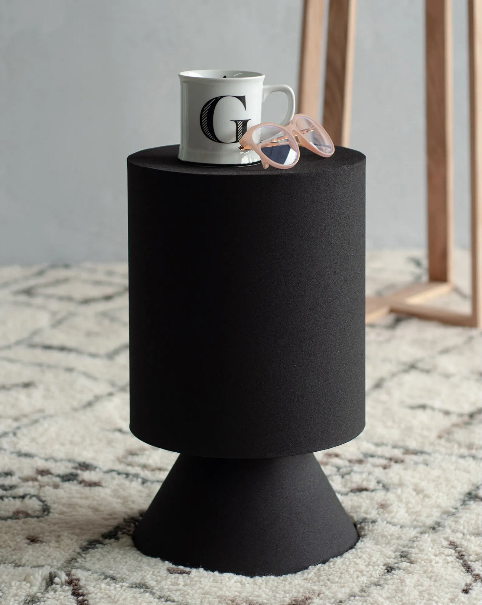 Atlas black sculptural side table styled on a textured rug with a coffee mug and glasses, showcasing its functional surface area.